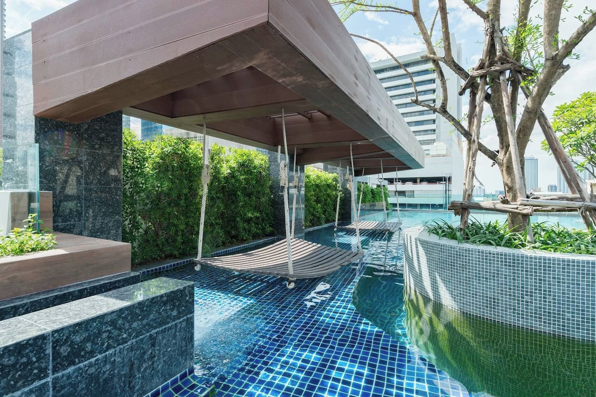 An indoor swimming pool with a modern design, surrounded by greenery and a covered seating area.