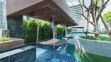 An indoor swimming pool with a modern design, surrounded by greenery and a covered seating area.