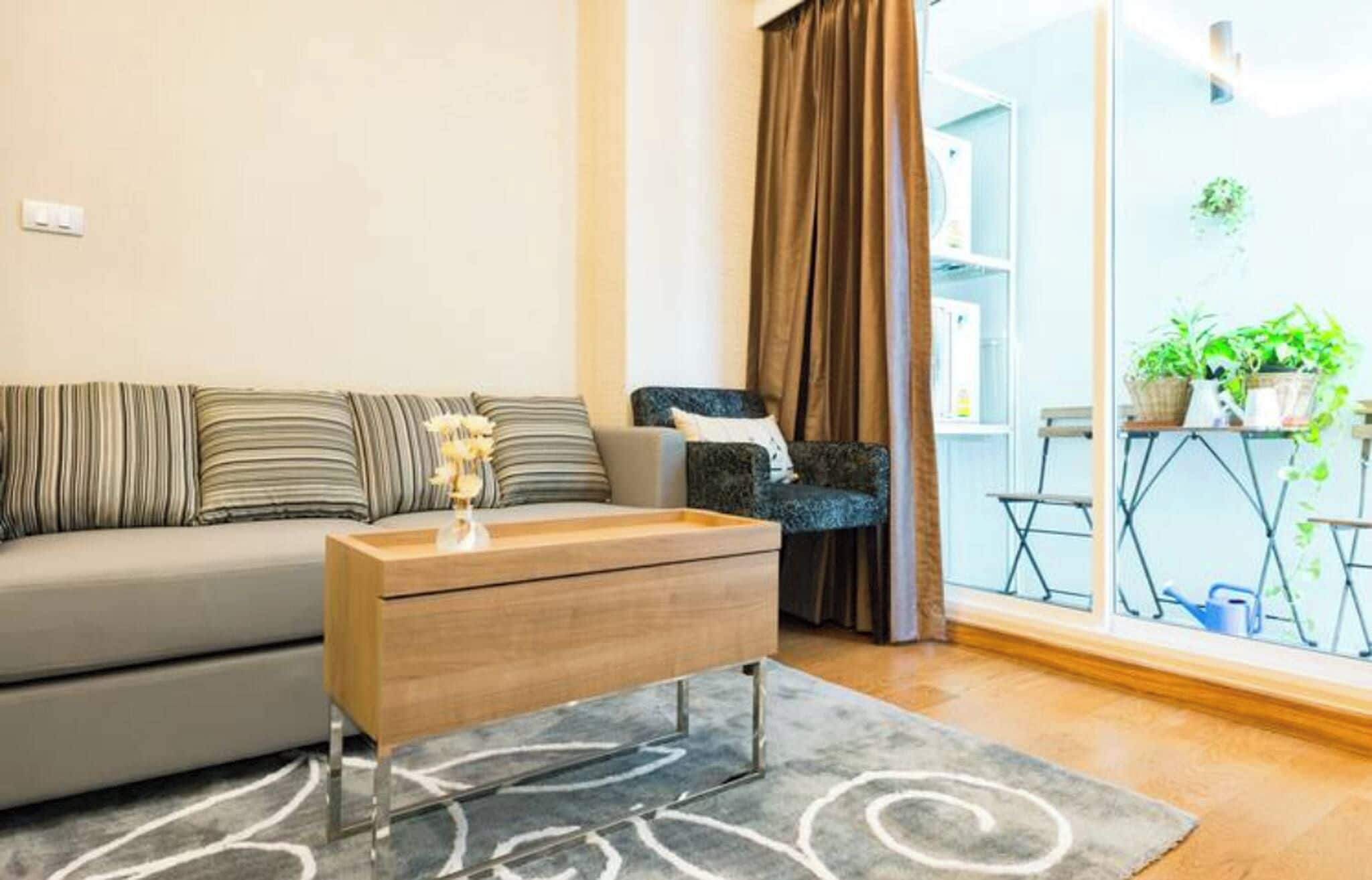 A modern living room with a sofa, a side table, and a view of a balcony with plants.