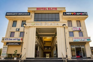 Un edificio de varios pisos con una entrada destacada que dice 'MB PLAZA' y varios letreros de negocios, incluyendo 'HOTEL ELITE', 'SIDDHARTH INFRATECH' y 'MOV SPORTS'.