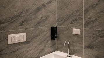 A bathroom with a marble wall, a pedestal sink, a wall-mounted faucet, and a light switch.