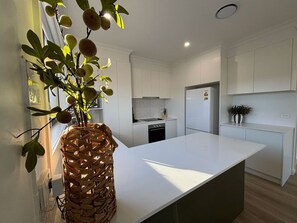 A modern kitchen with white cabinetry, a large island, and a woven basket with fruit.