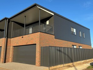 A modern two-story building with a brick facade, a flat roof, and a covered balcony.