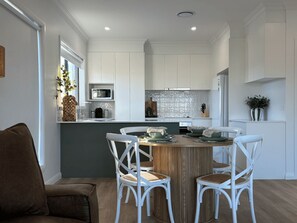 Une cuisine moderne avec des meubles blancs, un îlot central doté de sièges et un coin repas avec des chaises blanches.