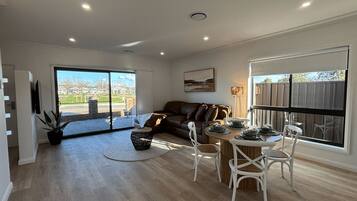 A spacious living area with a large window, a sofa, a dining table with chairs, and a potted plant.
