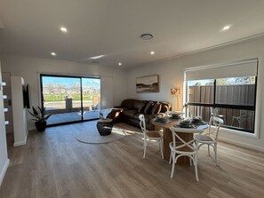 A spacious living area with a large window, a sofa, a dining table with chairs, and a potted plant.