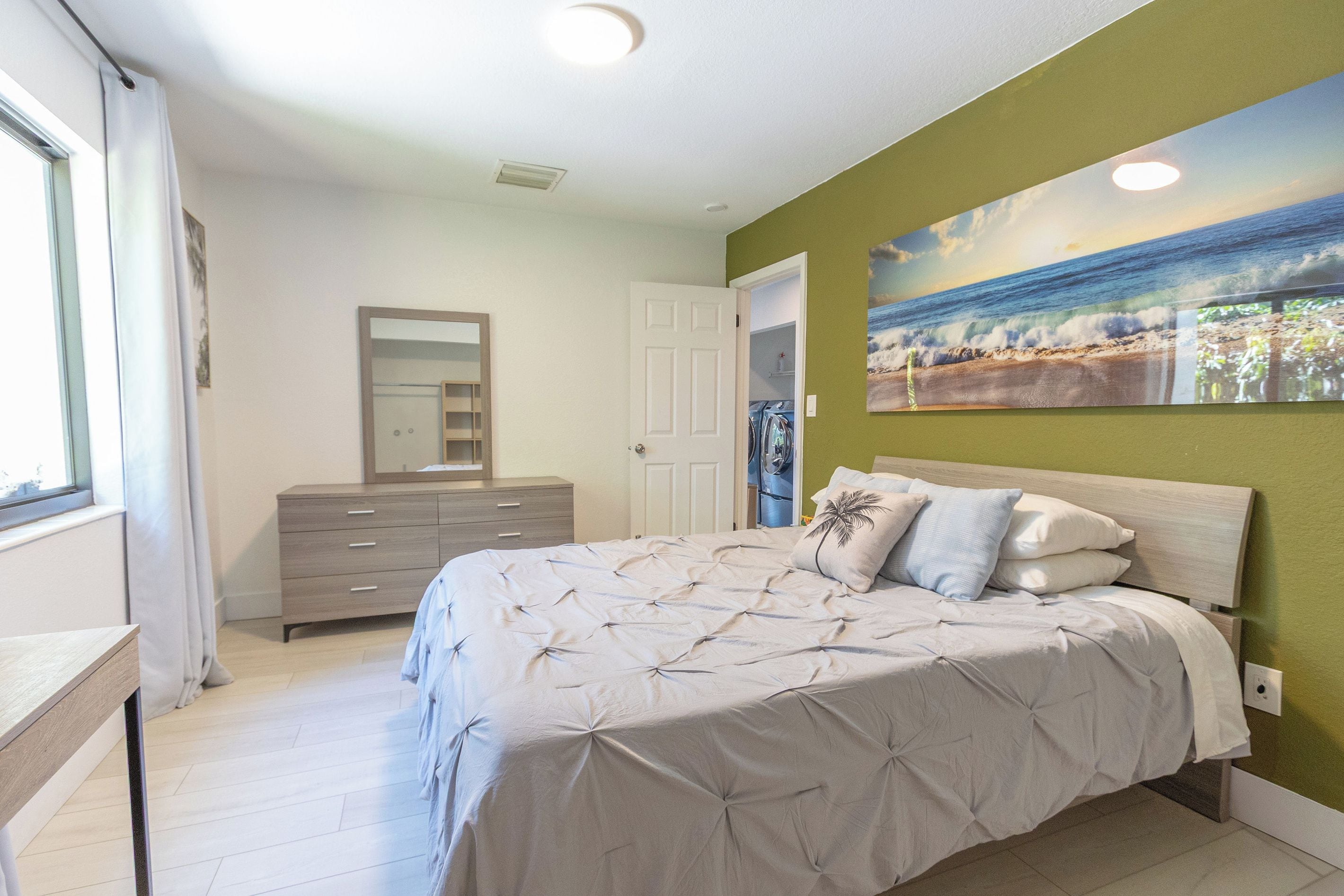 A bedroom with a bed, a dresser, a mirror, and a painting on the wall.