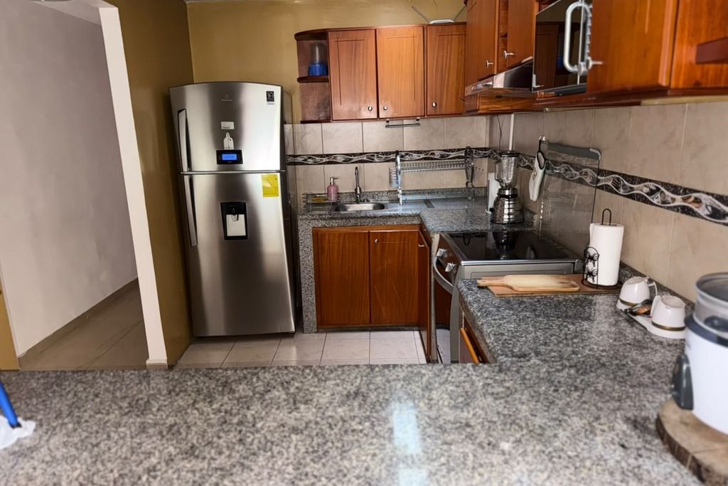 Una cucina con piani di lavoro in granito, elettrodomestici in acciaio inossidabile, mobili in legno e zoccolo schienale piastrellato.
