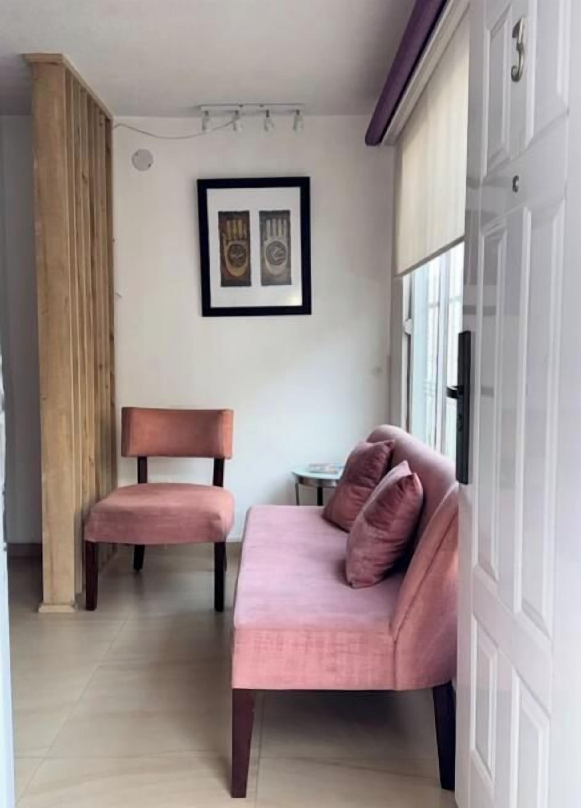Une pièce avec un canapé rose, une chaise en bois et une petite table.