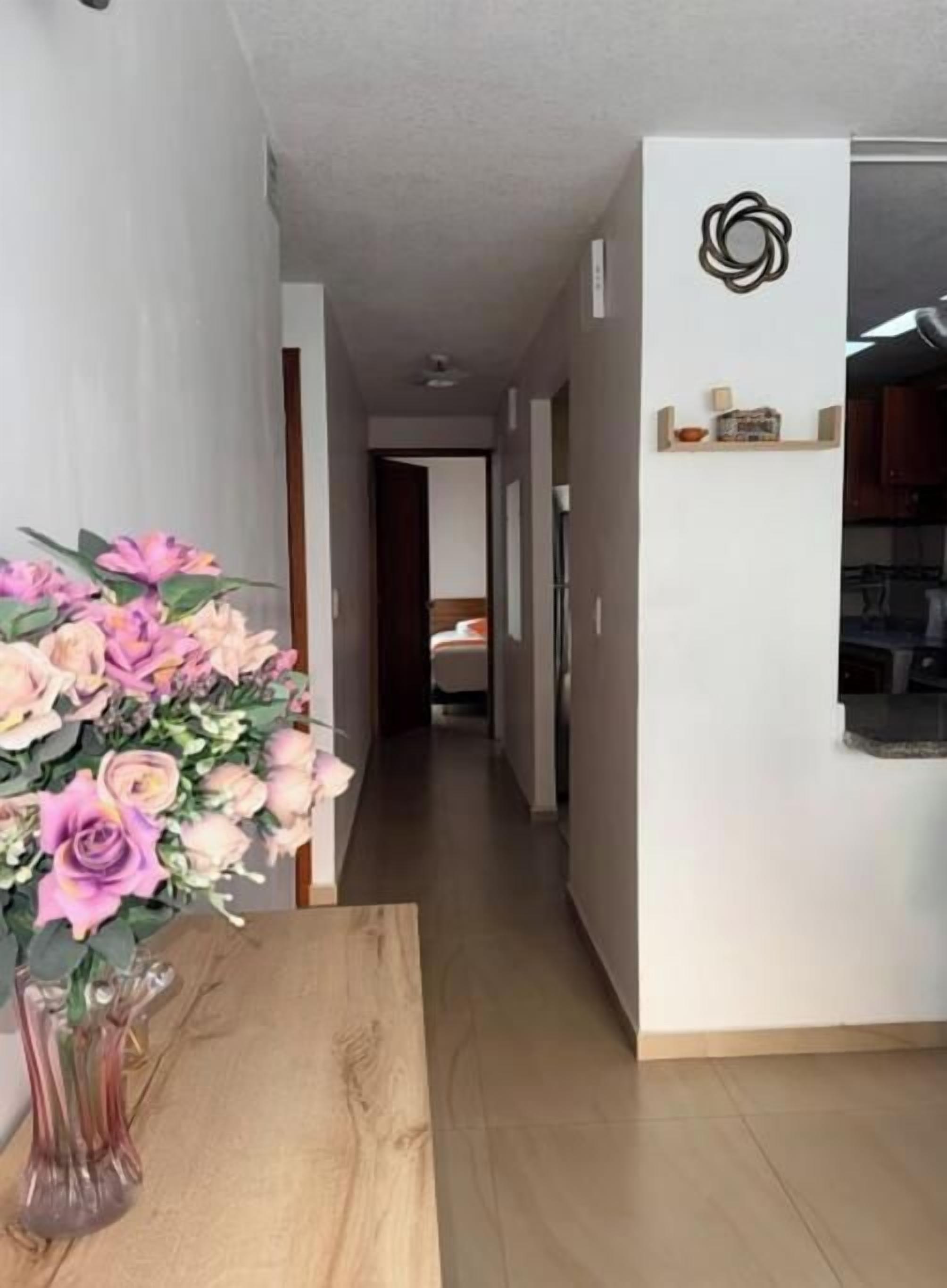 Un couloir avec une table en bois et un vase de fleurs, qui mène à un espace cuisine.
