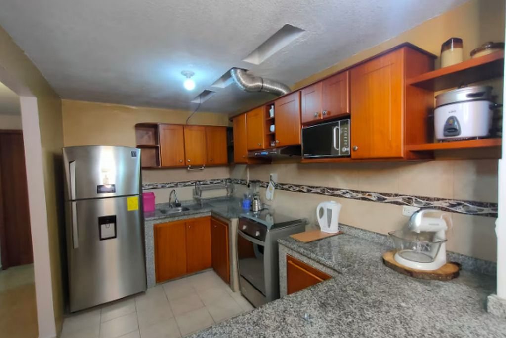Una cocina con armarios de madera, un refrigerador de acero inoxidable, un microondas y una cafetera.