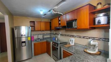 Una cocina con armarios de madera, un refrigerador de acero inoxidable, un microondas y una cafetera.