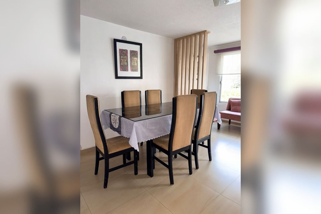 A dining area with a table and chairs, a framed picture on the wall, and a window with curtains.