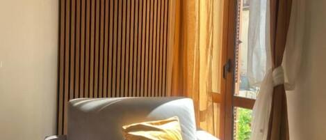 Una habitación con sofá, ventana con cortinas y un panel de madera en la pared.