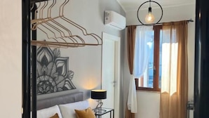 A hotel room with a bed, a bedside table with a lamp, a wall-mounted air conditioner, and a window with curtains. - MARMORE GREEWAY (Collestatte Piano)