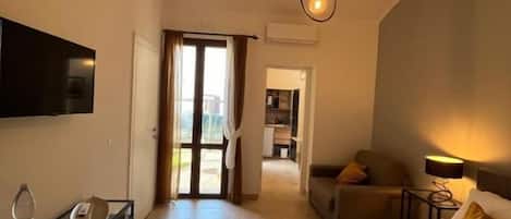 Habitación de hotel con cama, escritorio, silla, televisor y puerta que da a un balcón.