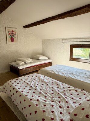 Un dormitori amb dos llits, un panell de capçal de fusta, una finestra i un quadre penjat a la paret.