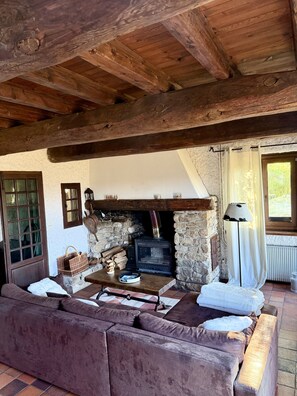 A rustic interior with a stone fireplace, wooden beams, a sofa, and a window with curtains. - Maison Aline - Maison familiale avec vue sur les montagnes (Font-Romeu-Odeillo-Via)
