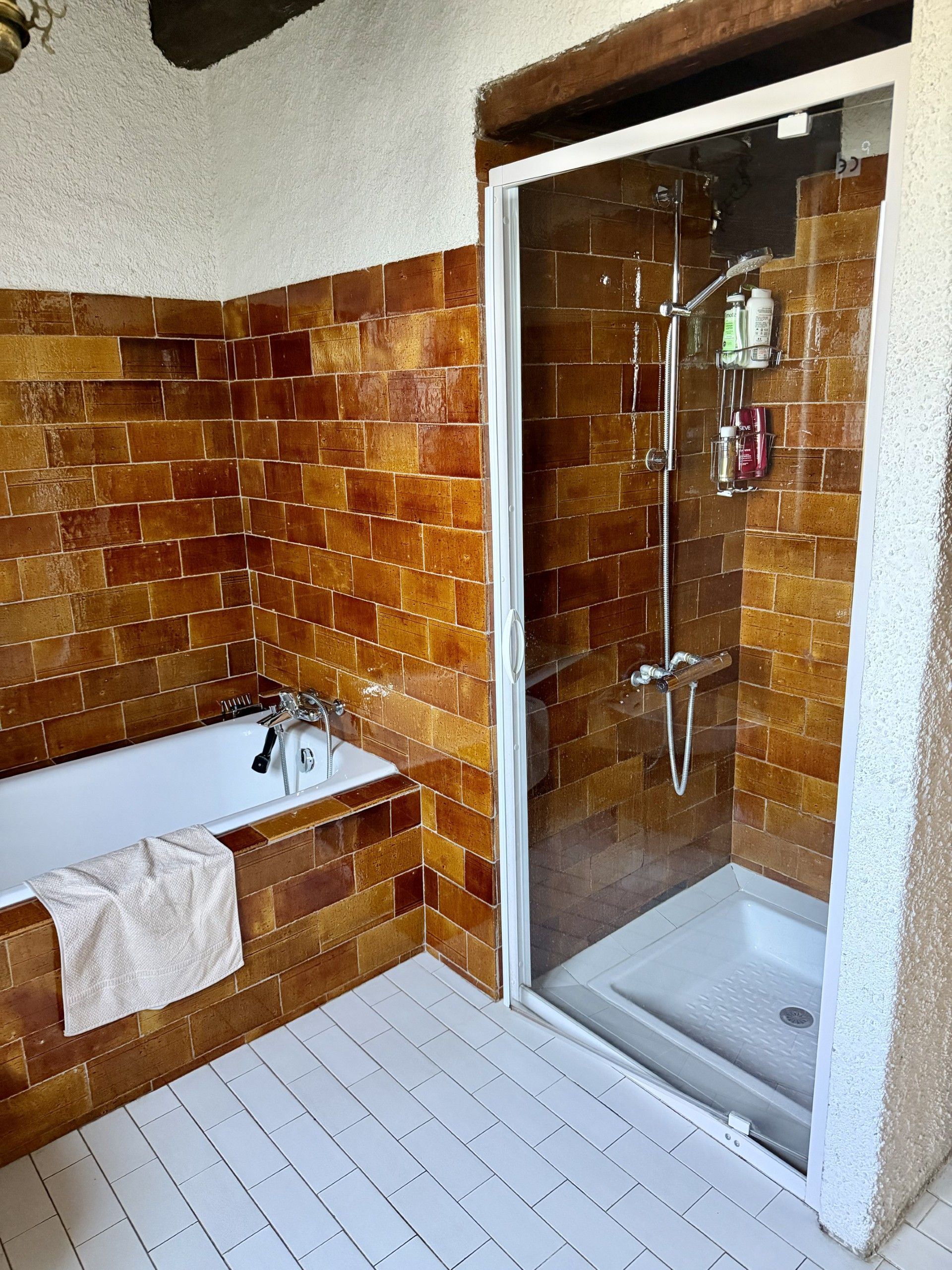 Ein Badezimmer mit Badewanne, Dusche und gefliestem Boden in Weiß.
