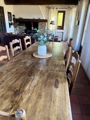 A rustic dining table with a vase of greenery, wooden chairs, and a stone fireplace in the background. - Maison Aline - Maison familiale avec vue sur les montagnes (Font-Romeu-Odeillo-Via)