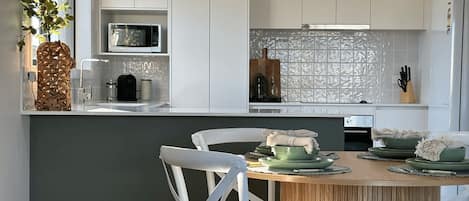 A modern kitchen with white cabinets, a microwave, and a dining area with a wooden table and chairs.