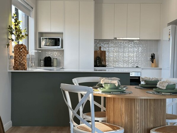 A modern kitchen with white cabinets, a microwave, and a dining area with a wooden table and chairs.