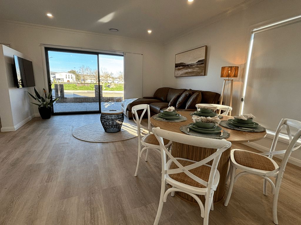 Un coin repas avec une table en bois dressée pour quatre personnes, entourée de chaises blanches.