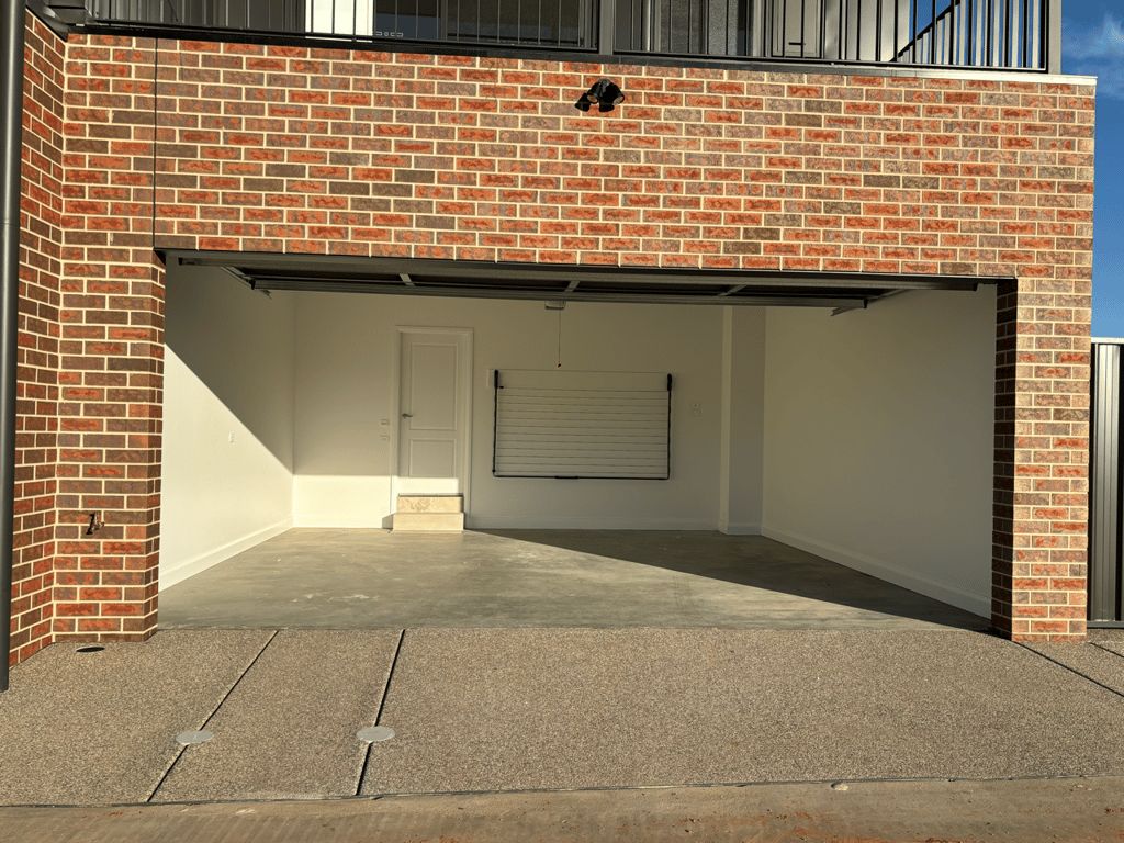 A garage with a closed roller door, brick walls, and a concrete floor.