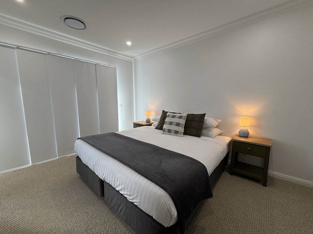 Een slaapkamer met een bed, nachtkastjes, een lamp en een kledingkast.