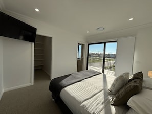 Quarto com cama, almofadas, mesa de cabeceira, janela e vista para o exterior.