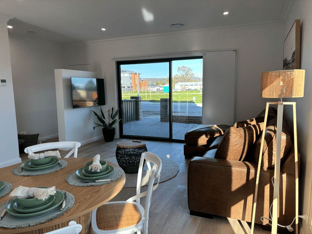 A modern living room with a dining area, a sofa, and a television mounted on the wall.