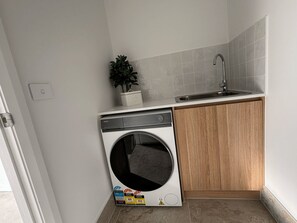 A compact kitchen with a built-in washing machine, a sink, and a potted plant.