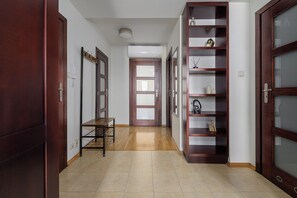 A hallway with wooden doors, a metal-framed table, and a shelving unit with decorative items. - Lumina 3r Apart w/ AC, Parking, Balcony (Warszawa)