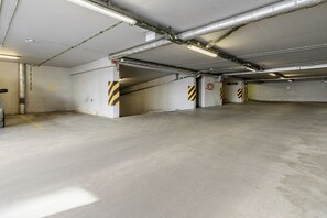 A parking garage with concrete floors, yellow and black striped safety markings, and visible fire extinguishers. - Lumina 3r Apart w/ AC, Parking, Balcony (Warszawa)