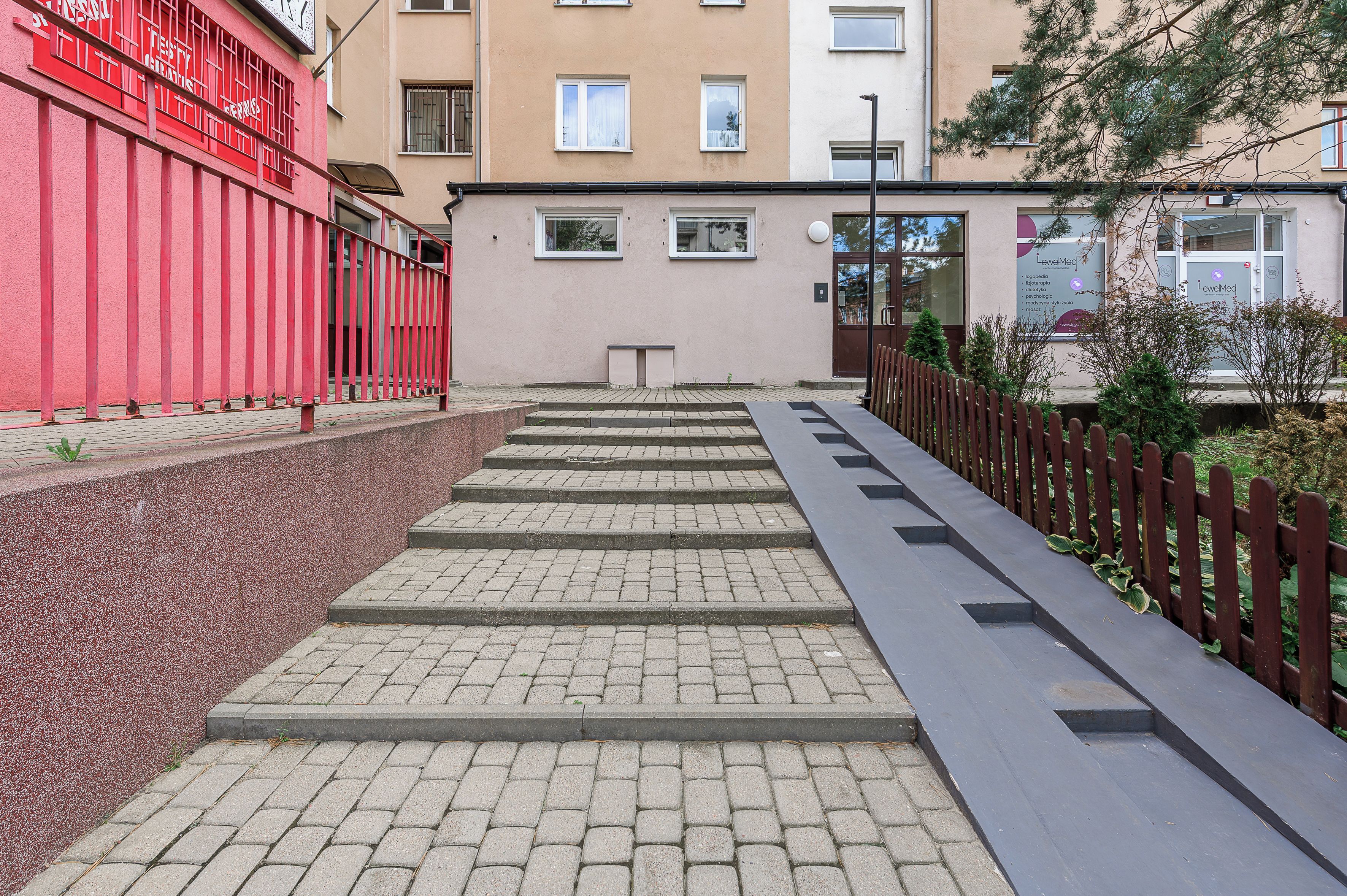 A set of outdoor stairs leading to a building entrance, with a red fence on the left and a wooden fence on the right.