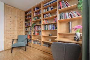 A room with a wooden bookshelf filled with books, a grey armchair, and a small table with a vase of flowers. - Lumina 3r Apart w/ AC, Parking, Balcony (Warszawa)
