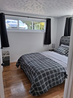 A bedroom with a bed, a nightstand, a lamp, a window with curtains, and a view of the outside.