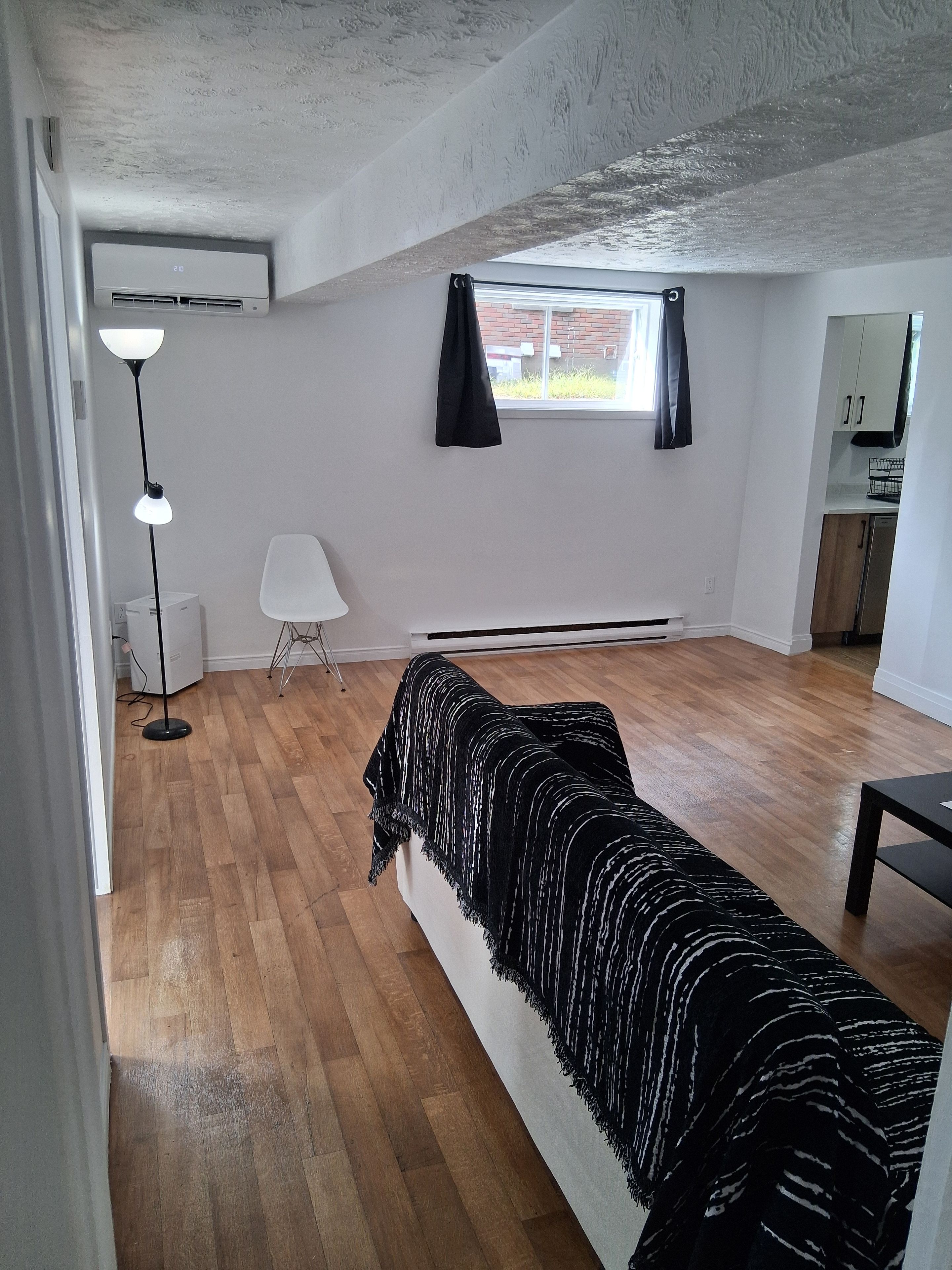 Een kamer met een bed, een staande lamp, een stoel, een raam met gordijnen en een keukenhoek.