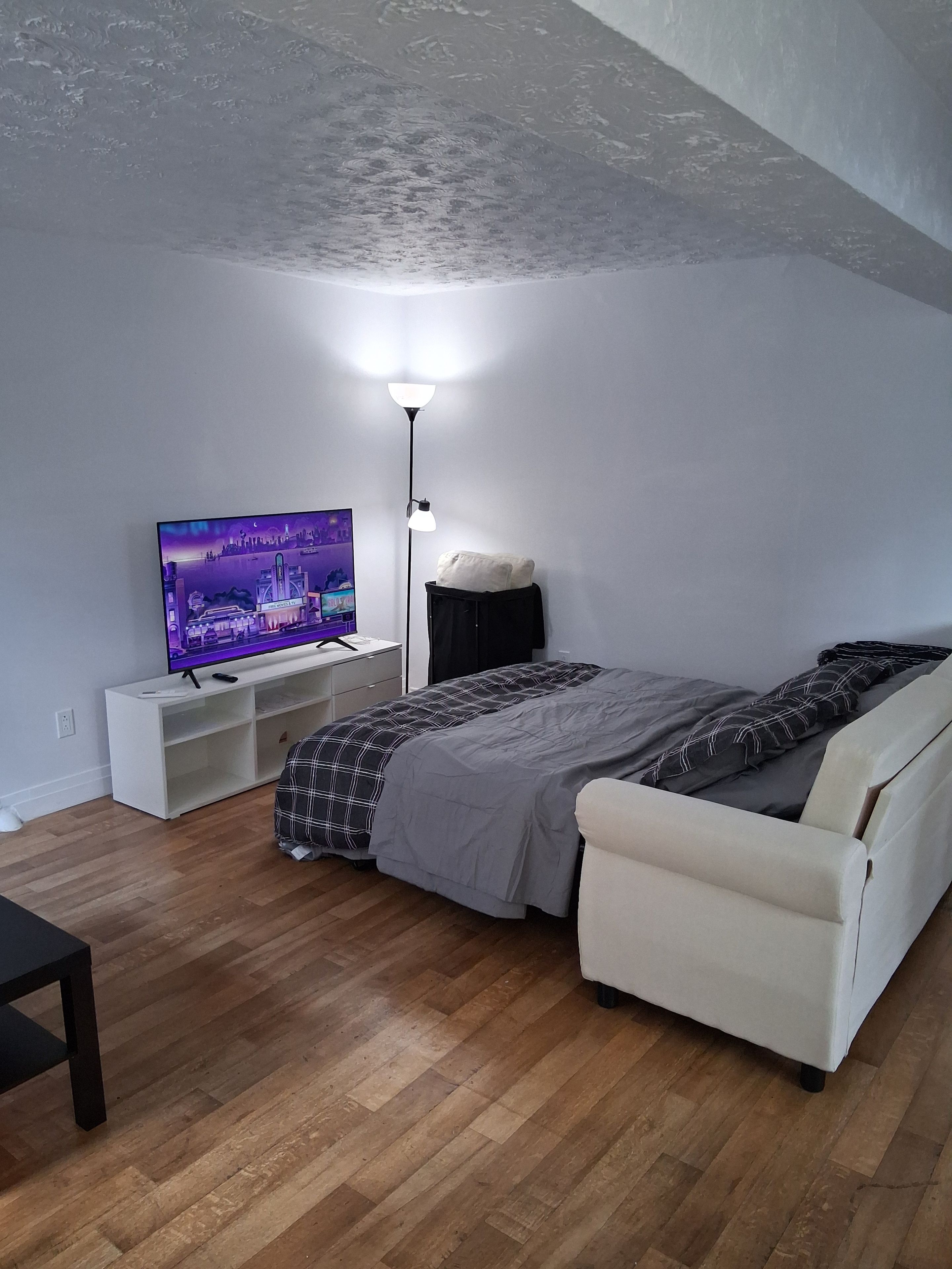 A modern bedroom with a bed, a TV, a floor lamp, and a white console unit.