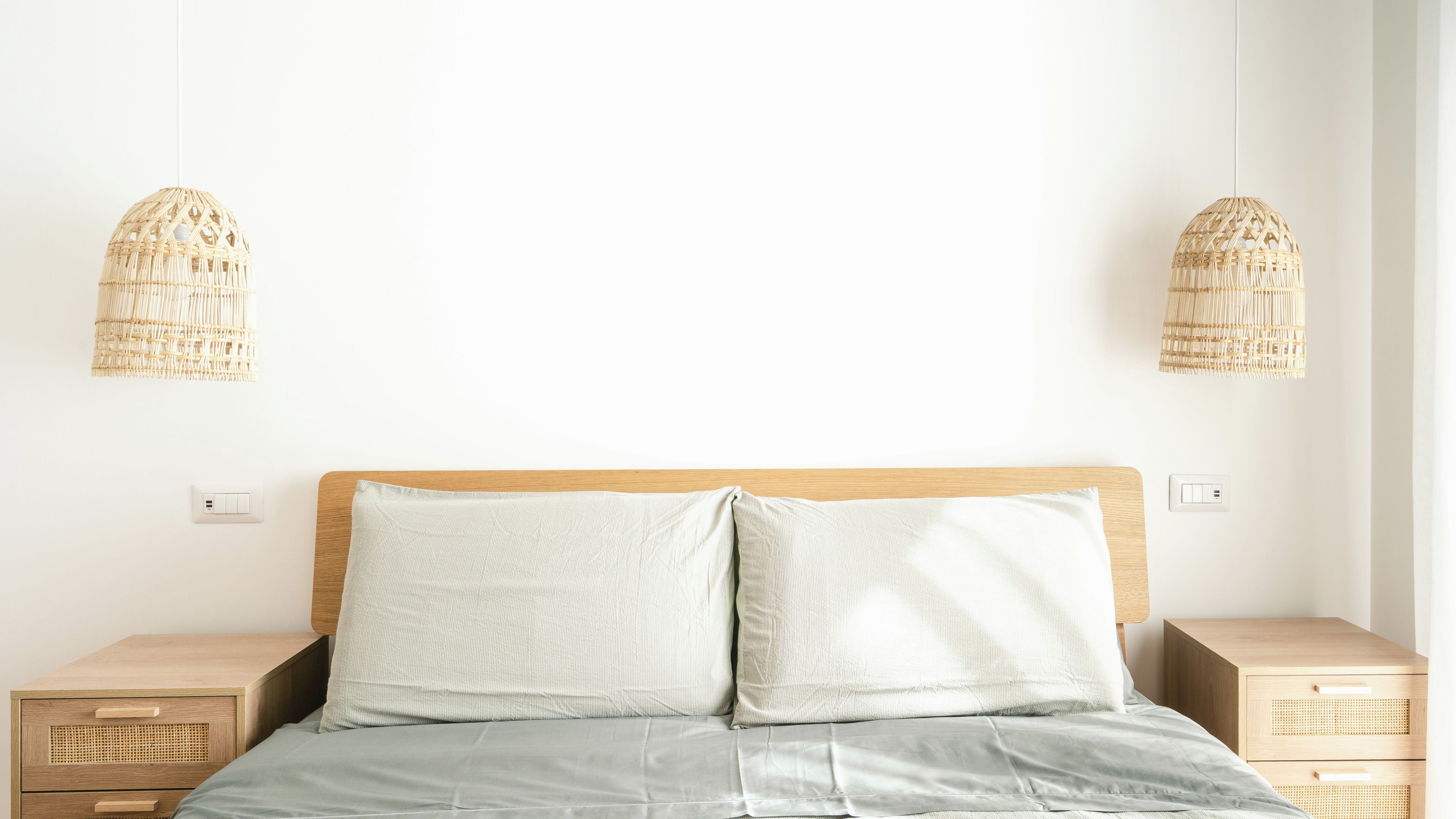 Een bed met een houten hoofdbord, twee nachtkastjes en twee geweven hanglampen.
