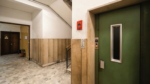 Um corredor com porta verde, parede de madeira, piso de mármore e um vaso com planta.