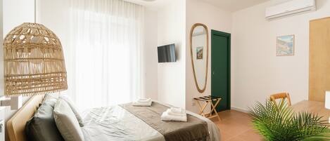 Una habitación de hotel moderna con una cama, un televisor, un espejo, una puerta y una planta.