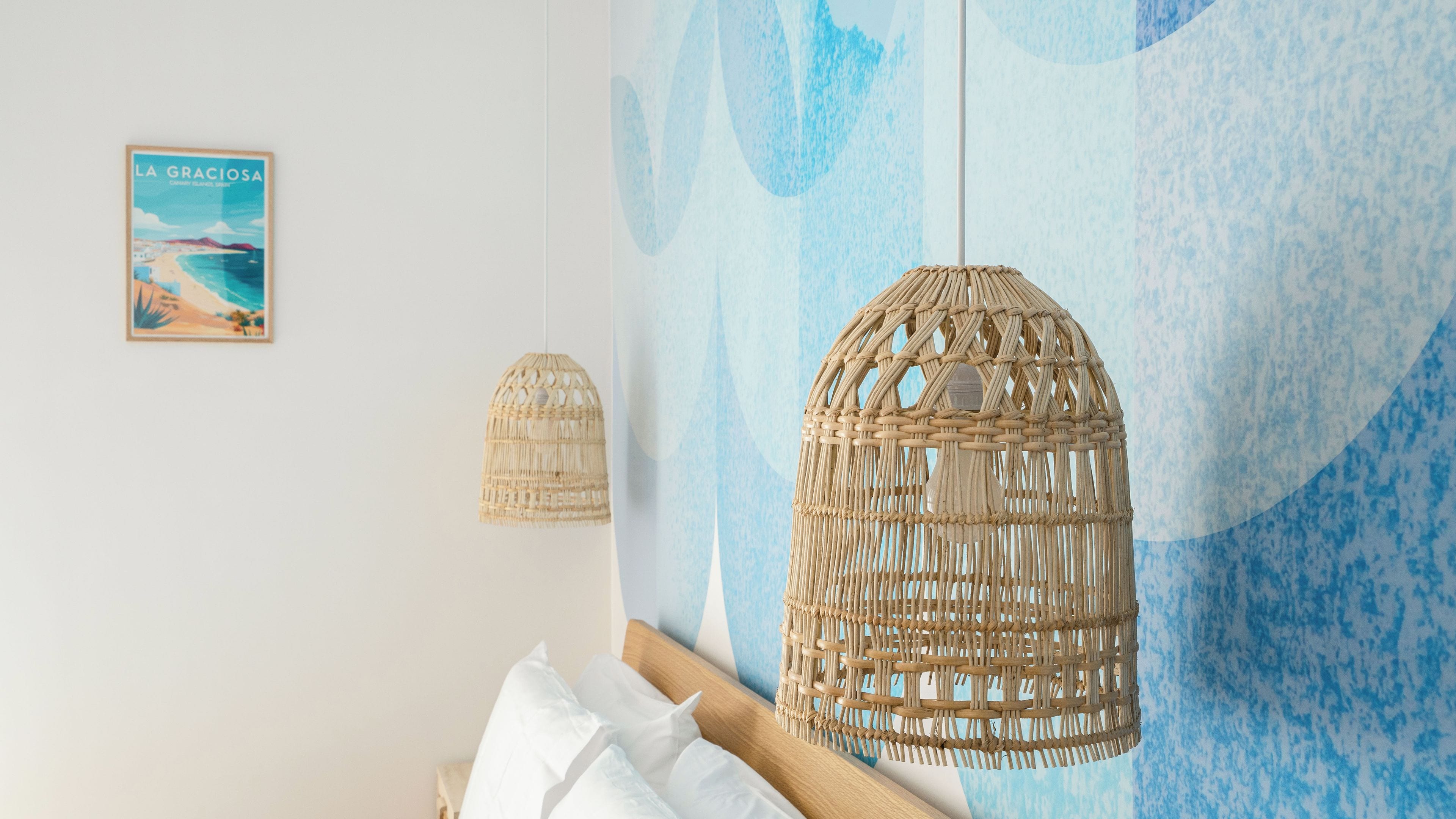 A bedroom with a bed, two woven light fixtures, a wall with a blue abstract design, and a framed picture on the wall.