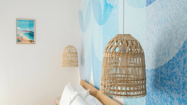 Un dormitorio con cama, dos lámparas de fibra natural, una pared con diseño abstracto azul y un cuadro enmarcado.