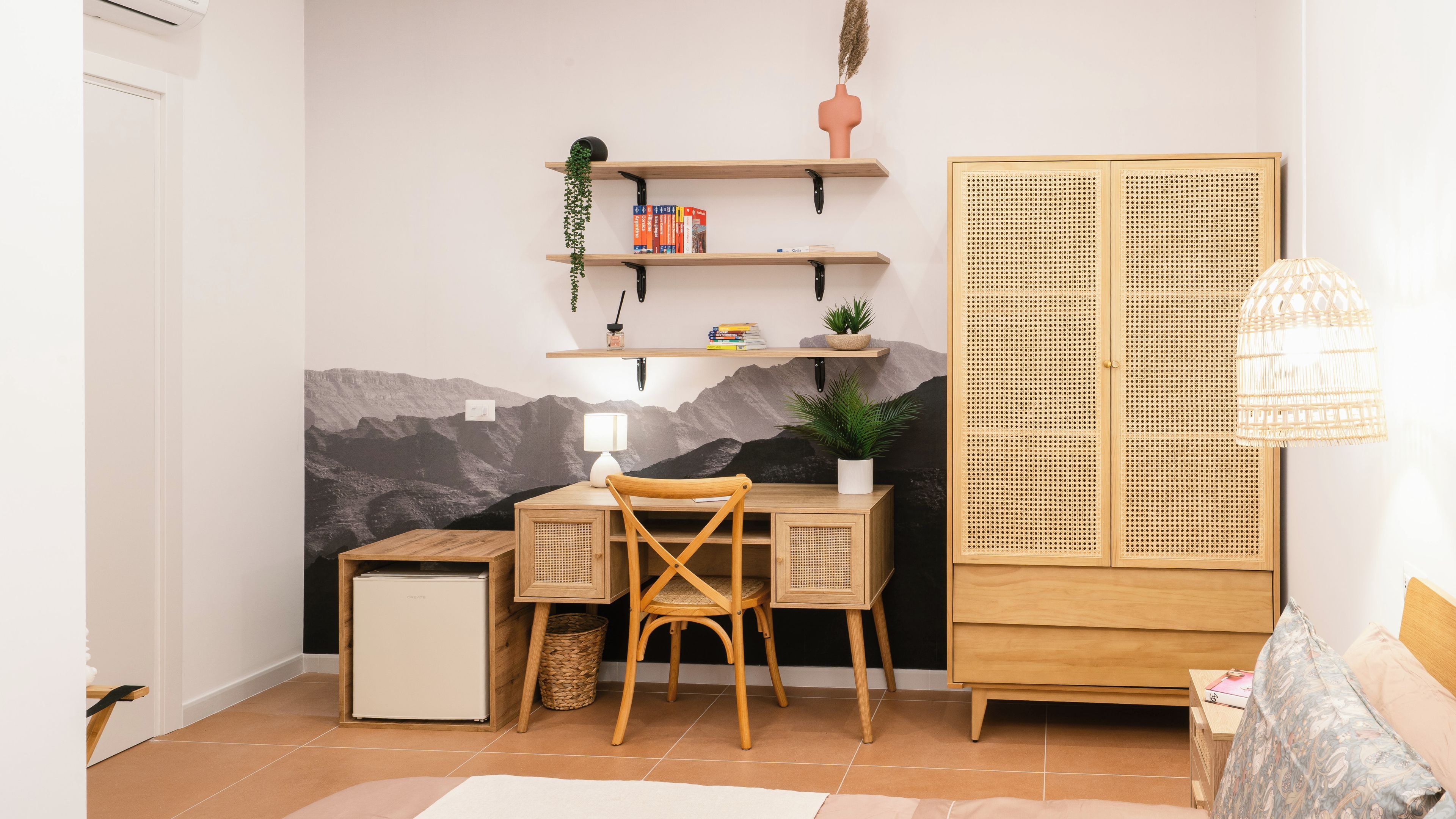 A room with a desk, chair, bookshelf, wardrobe, and a wall-mounted lamp.