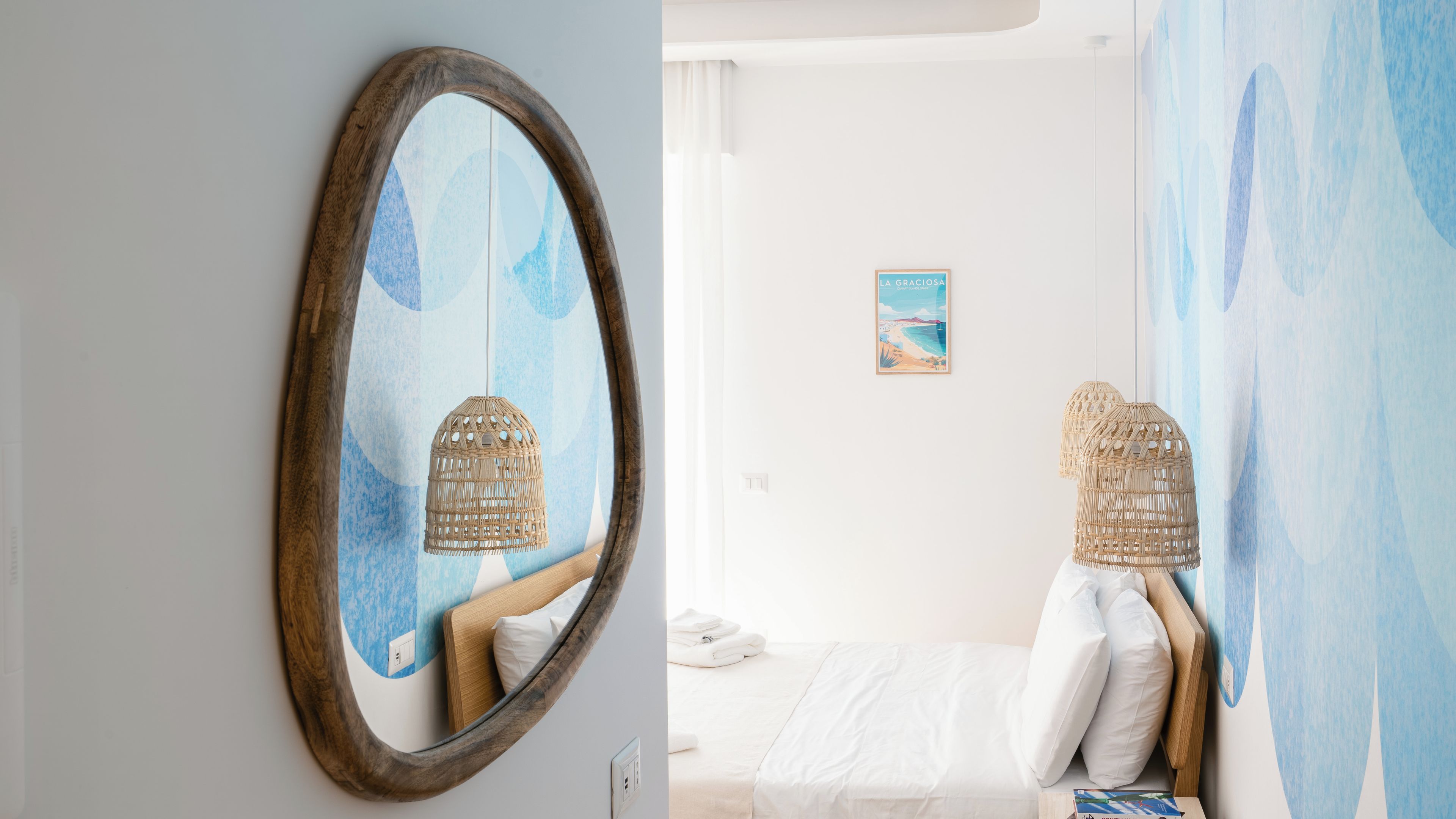 A room with a bed, a wall-mounted mirror, and a painting.