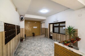 A hallway with a tiled floor, a wooden door, a mirror, and a potted plant. - Calima Guest House (Naples)