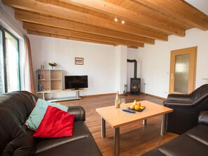Ein Wohnzimmer mit Holzbalkendecke, einem Fernseher, einem Kamin und einem Esstisch mit Obst.