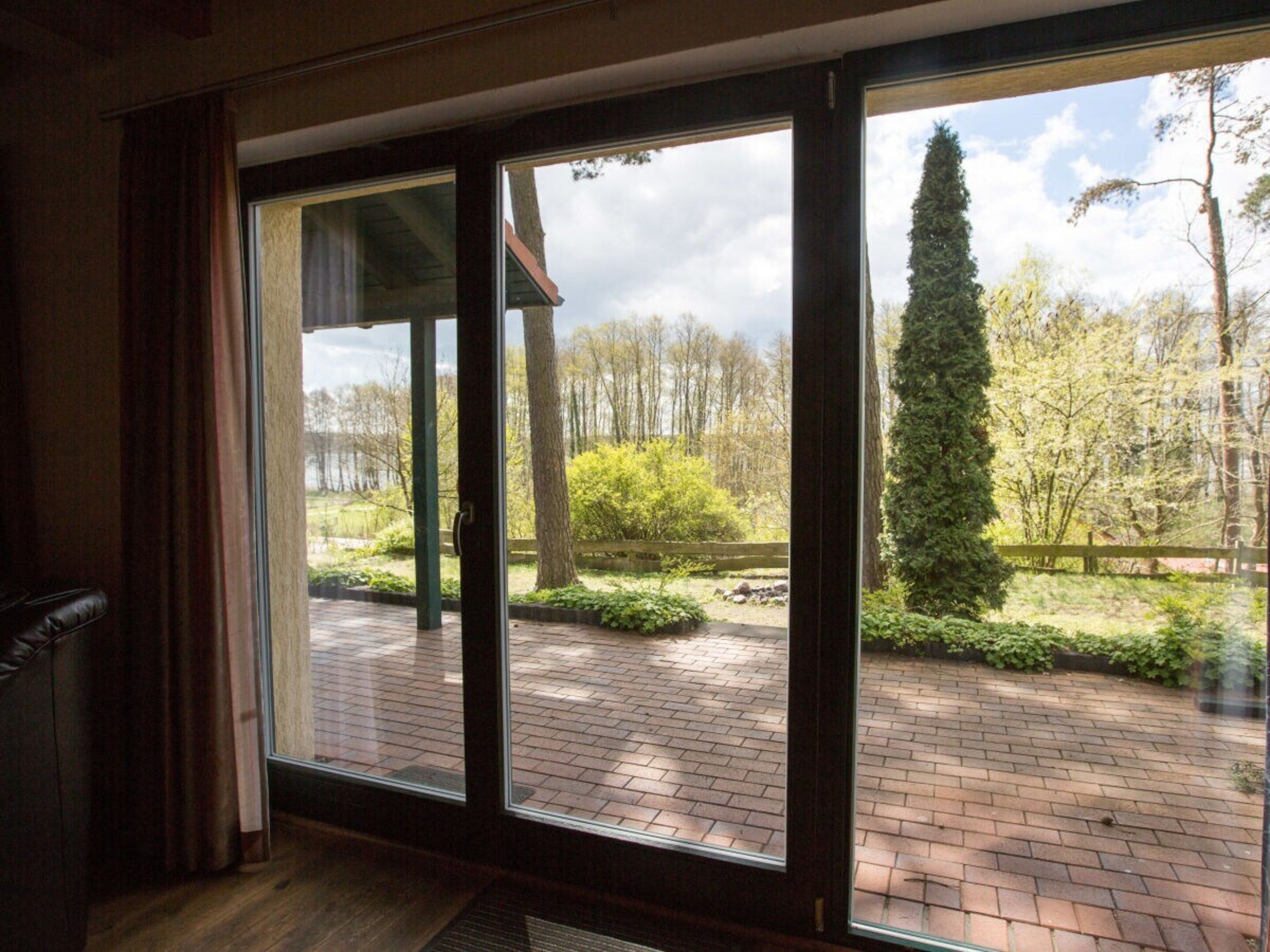 Een kamer met een grote schuifpui die uitkomt op een buitenruimte met een terras van baksteen en groen.