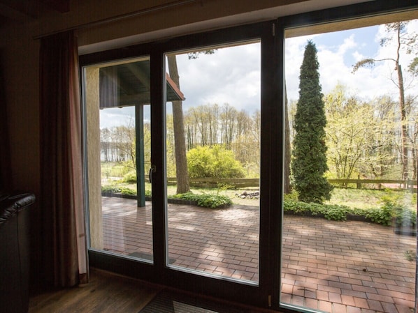 Ein Zimmer mit einer großen Schiebeglasdoor, die zu einem Außenbereich mit Pflasterterrasse und Grünflächen führt.